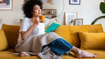 A woman sitting on a sofa, teacup and a book in her hands. A woman sitting on a sofa, teacup and a book in her hands.