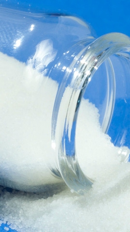 Ein Fläschchen mit weißem, superabsorbierendem Pulver, das auf ein blaues Tischtuch geschüttet wurde. Ein Fläschchen mit weißem, superabsorbierendem Pulver, das auf ein blaues Tischtuch geschüttet wurde.