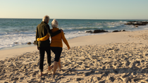 An elderly couple talking a walk on the beach.